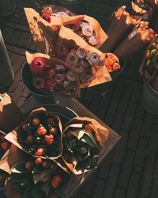 An assortment of flower bouquets and floral arrangements displayed outdoors on a wooden surface, featuring various flowers wrapped in brown kraft paper and arranged in black buckets and pots. The bouq